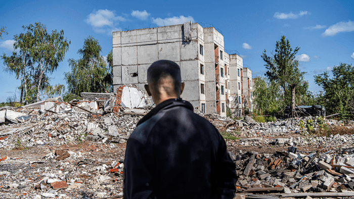 Mann mit dem Rücken zum Bild vor zerstörten Gebäuden